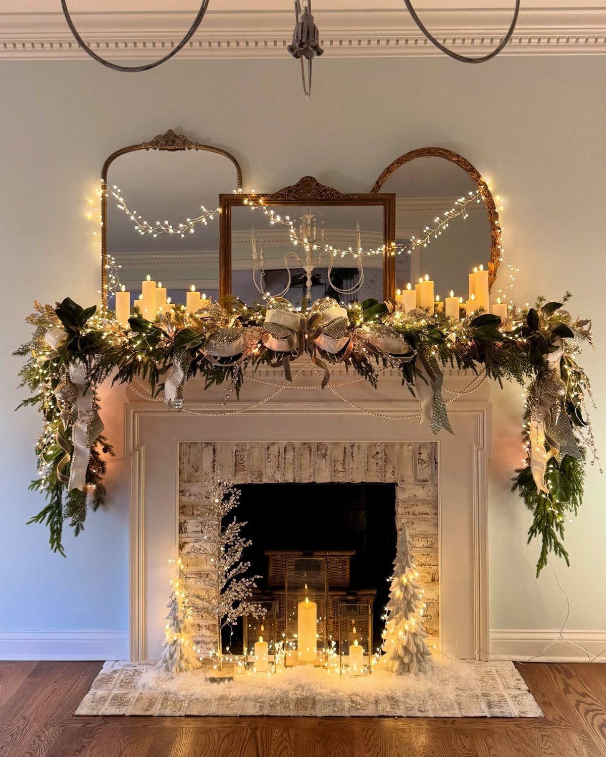 Decorated white fireplace mantel with green garlands, glowing candles, and fairy light mirrors.
