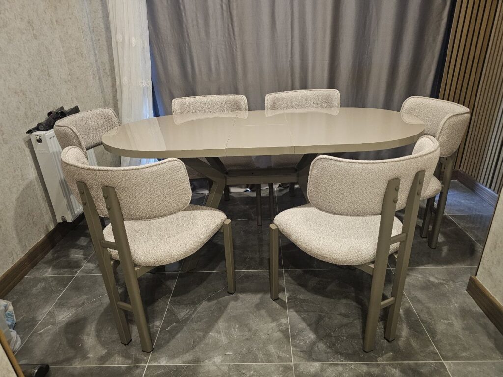 Oval beige dining table with six upholstered chairs on a grey tiled floor