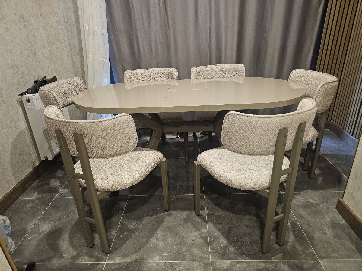 Oval beige dining table with six upholstered chairs on a grey tiled floor