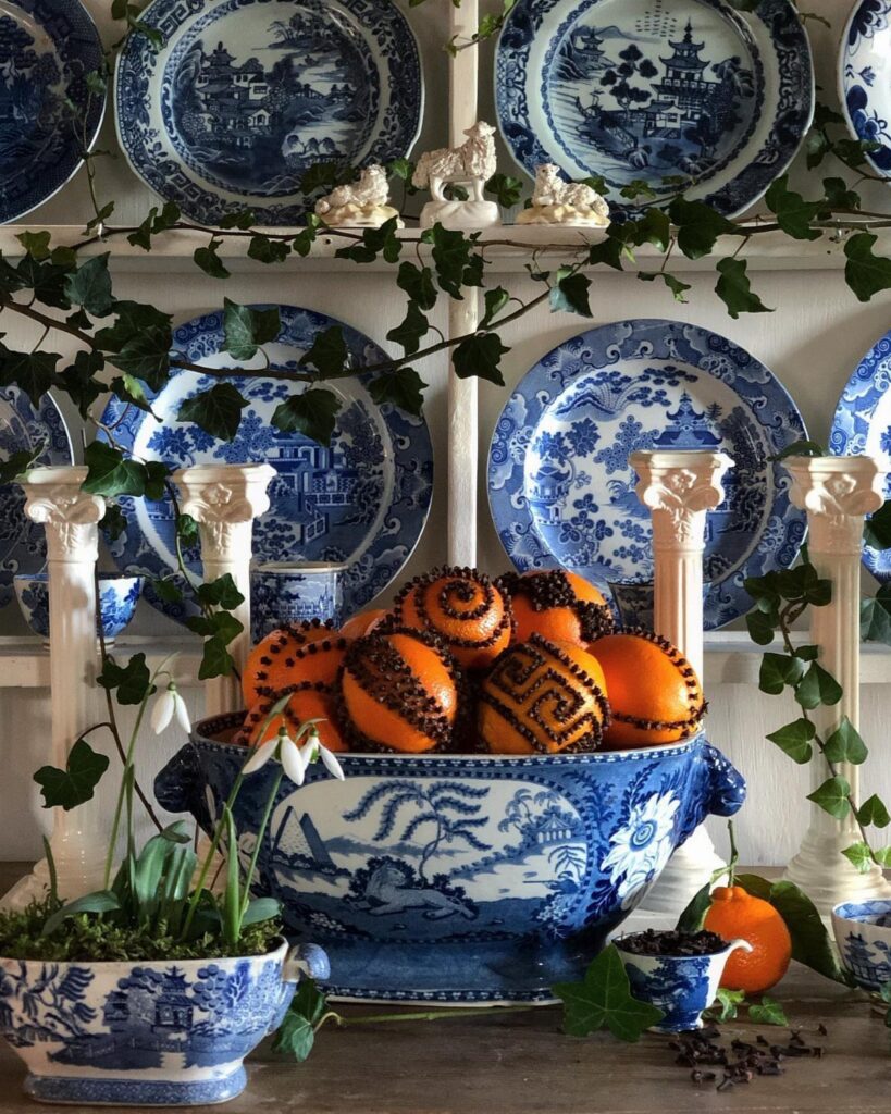 Cloves studded into oranges in a blue and white porcelain bowl with ivy.