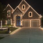 Brick house exterior decorated with warm white Christmas lights on roof and driveway