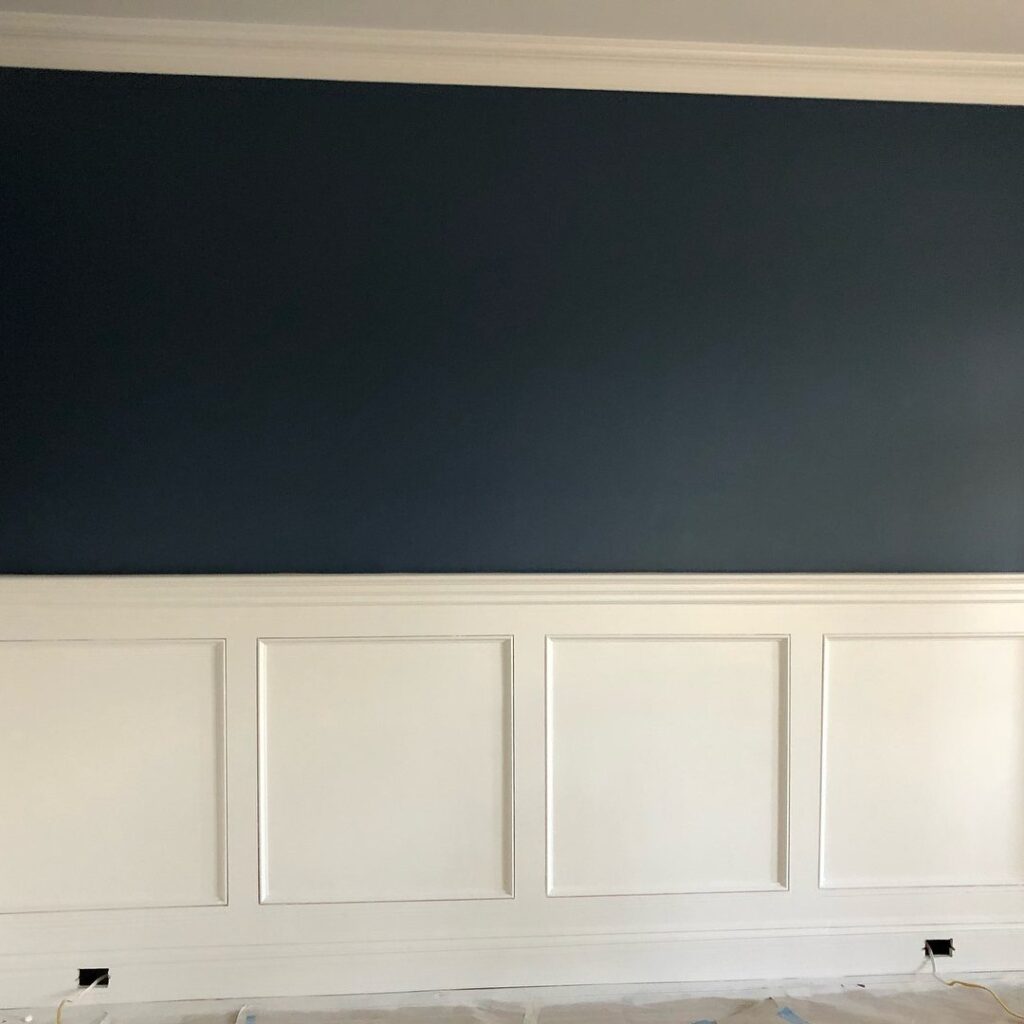 White wainscoting with square panels and a chair rail against a dark blue wall.