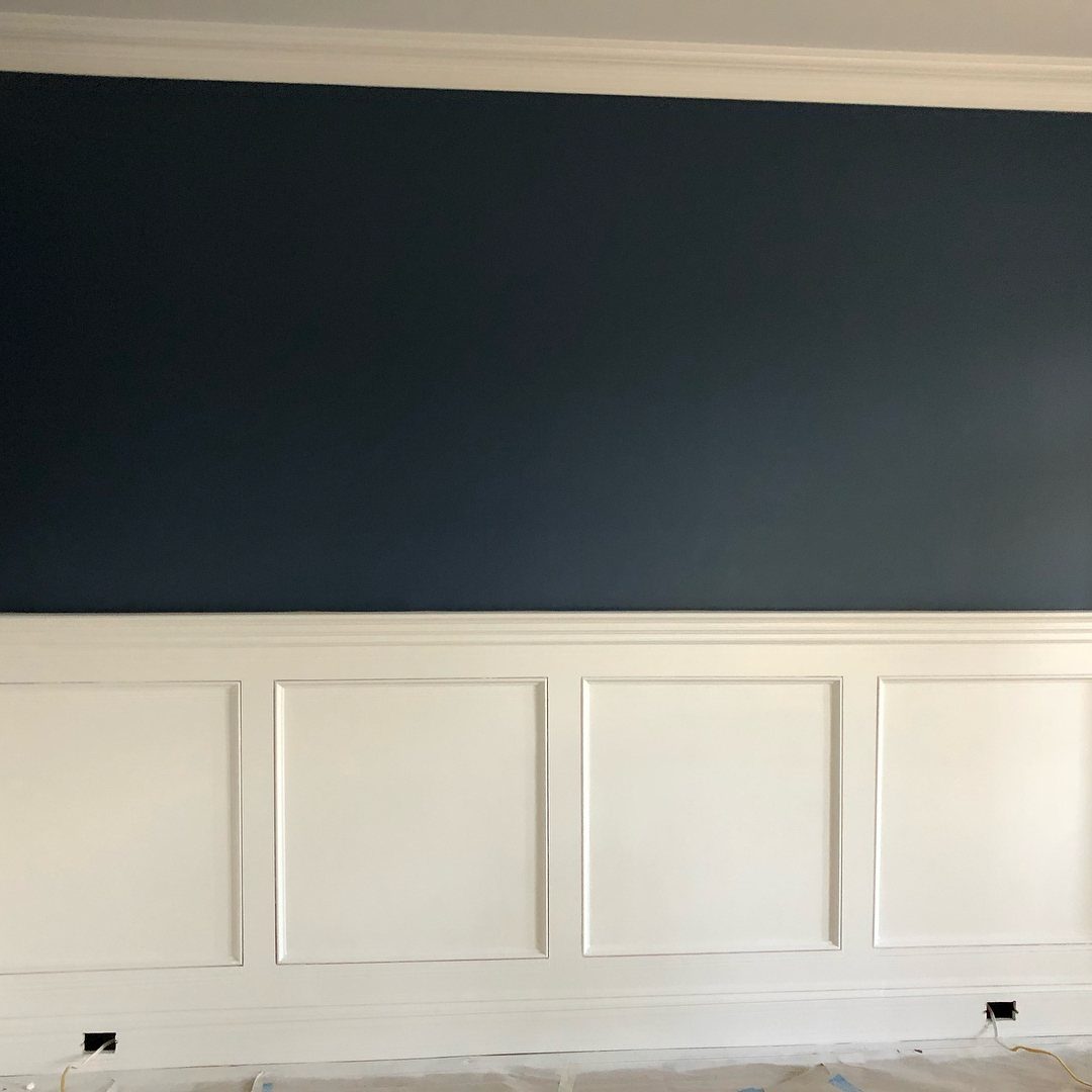 White wainscoting with square panels and a chair rail against a dark blue wall.