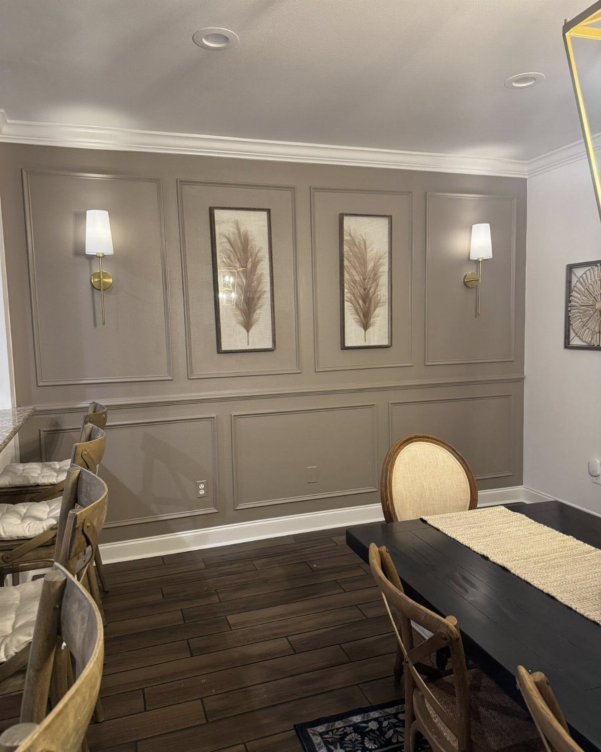 Taupe paneled dining room walls with gold sconces and a dark wood table.
