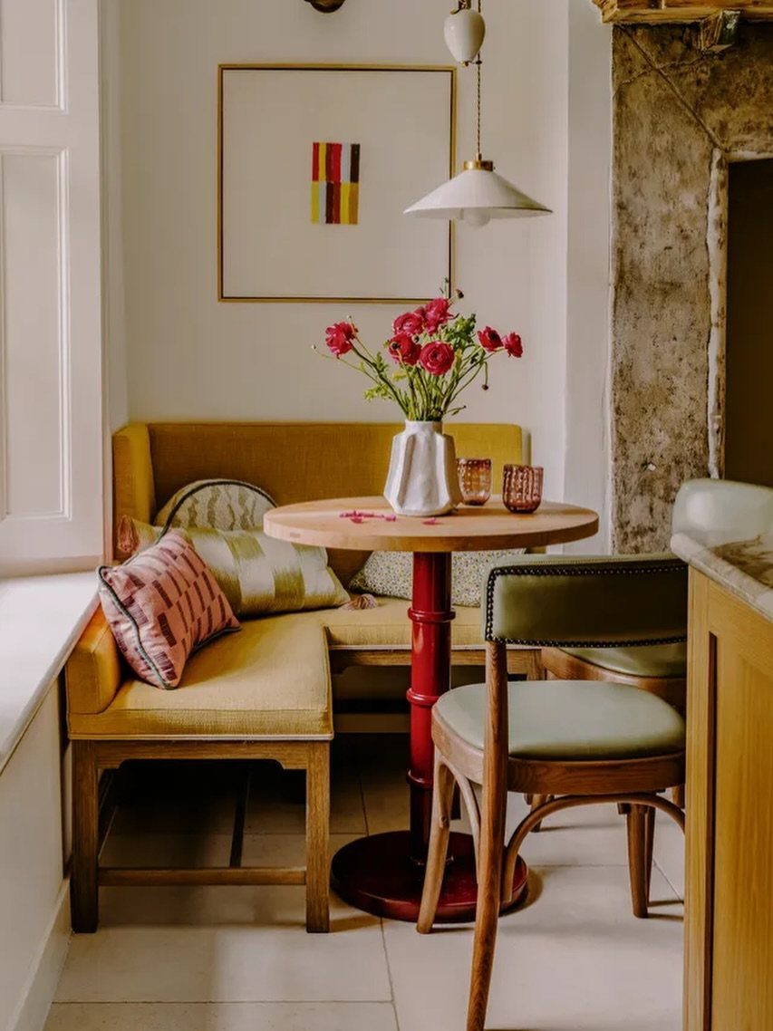 Yellow L-shaped banquette seating with a round wooden table and red flowers.