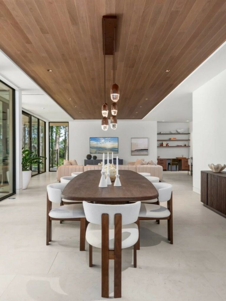 Wooden dining table with white chairs facing a beige sectional sofa in open-concept room