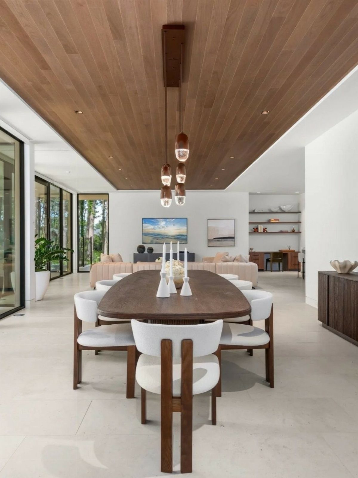 Wooden dining table with white chairs facing a beige sectional sofa in open-concept room
