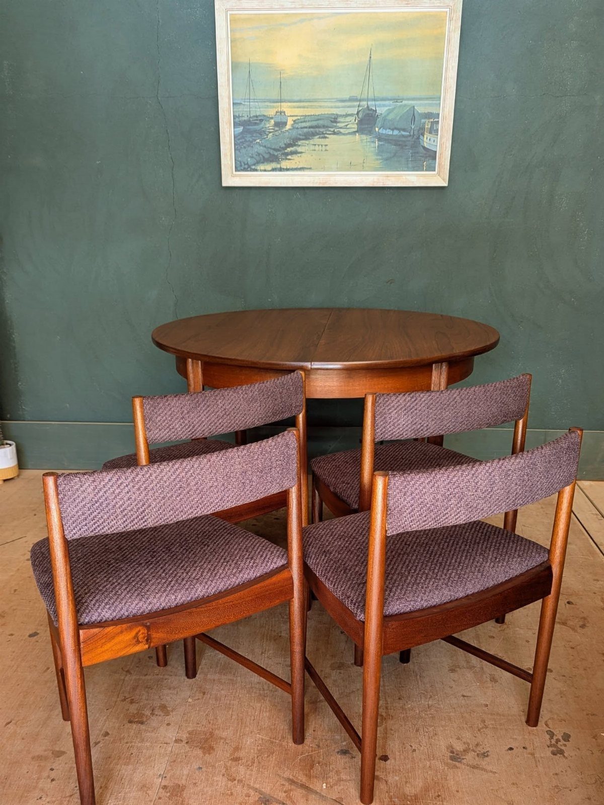 Round wooden dining table and four purple upholstered mid-century modern chairs against green wall