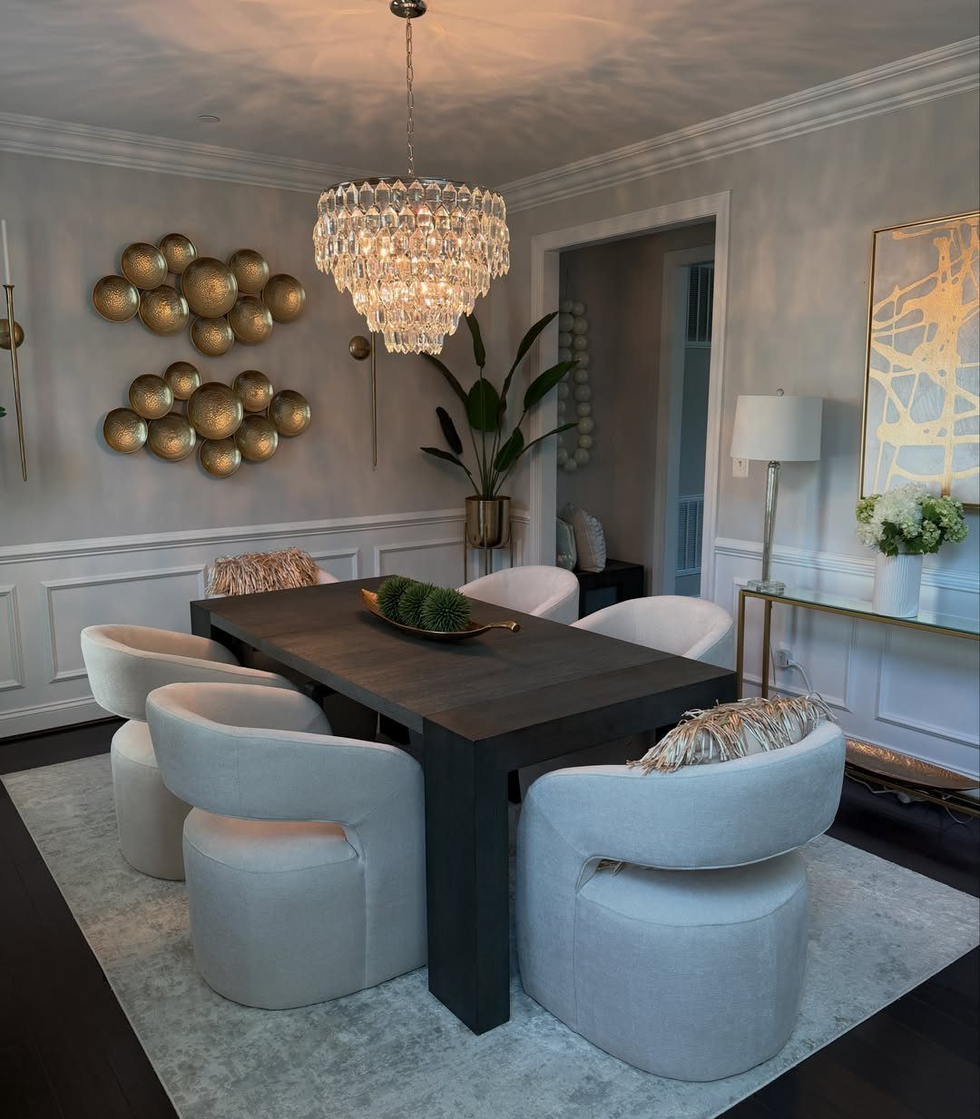 Dark wooden dining table with a gold centerpiece bowl and white curved chairs.