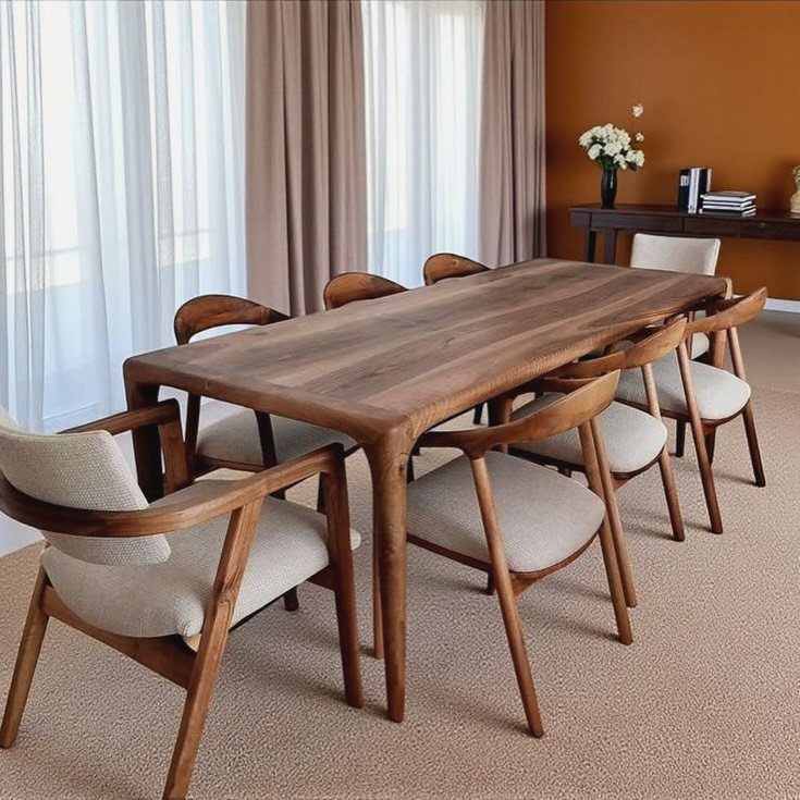 Wooden dining table with matching cushioned chairs in a bright, modern dining room.