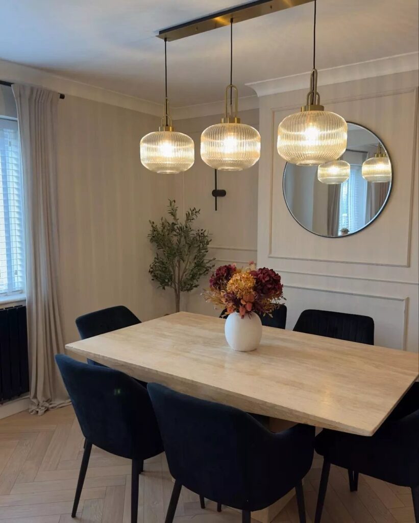 Three gold glass pendant lights hanging over a wooden dining table with blue chairs.