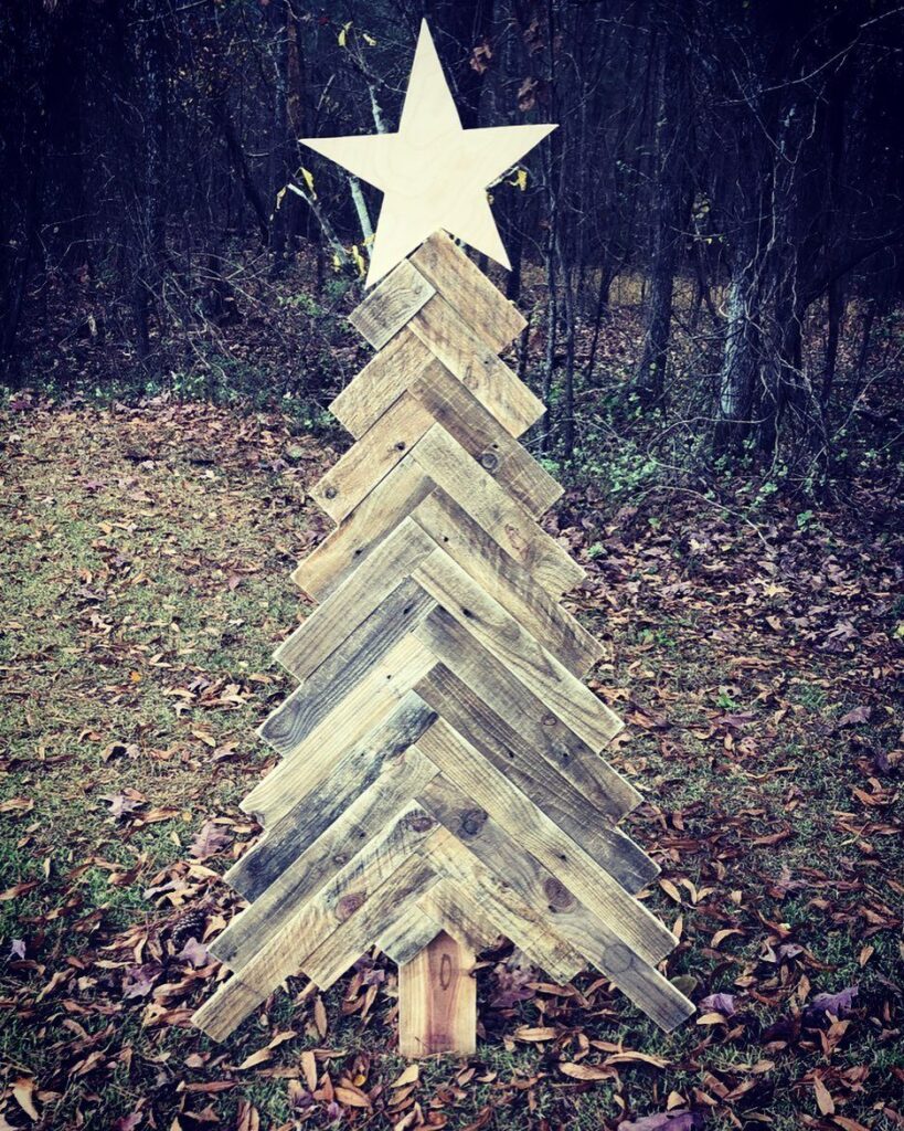 Wooden pallet Christmas tree with a star topper standing in autumn leaves.