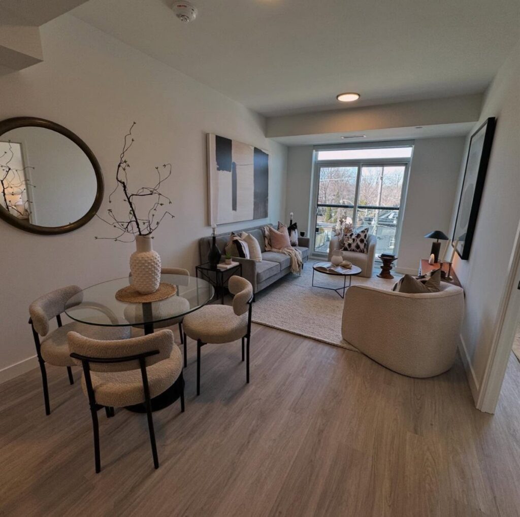 Open concept living and dining room with glass table and neutral toned furniture.