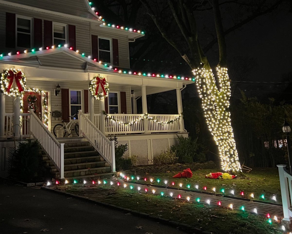 White house porch railing decorated with draped white lights and colorful roof lights.