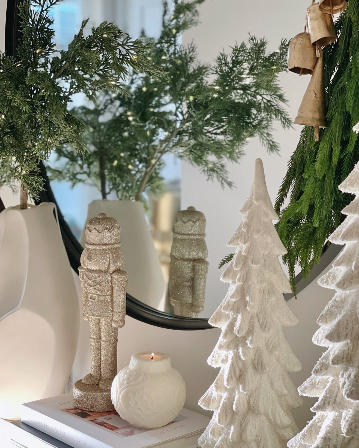 White and gold Christmas decorations with pine branches reflected in a round mirror.