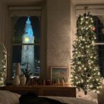 Lit Christmas tree and festive decorations in a room overlooking a city clock tower.