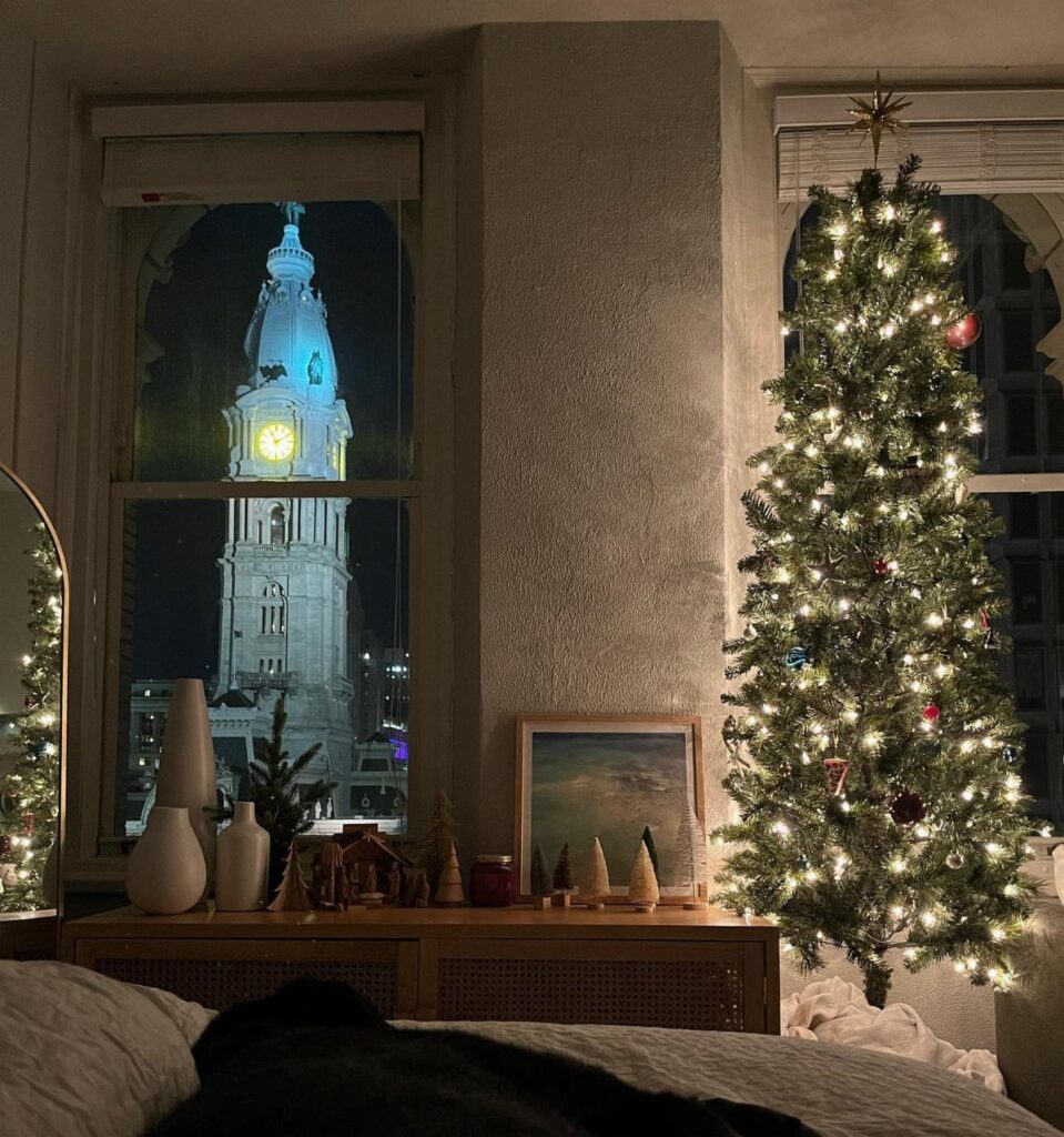 Lit Christmas tree and festive decorations in a room overlooking a city clock tower.
