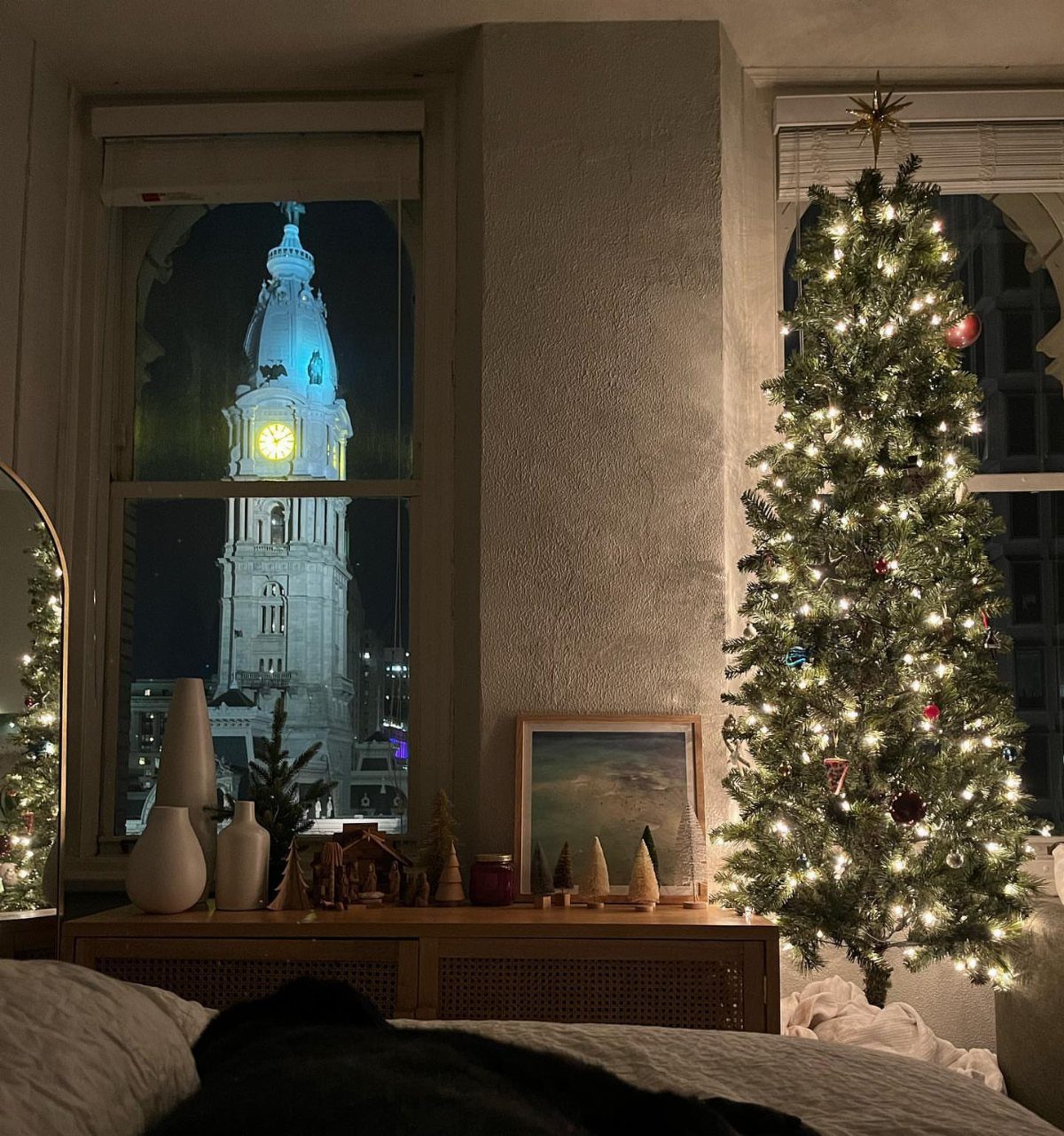 Lit Christmas tree and festive decorations in a room overlooking a city clock tower.