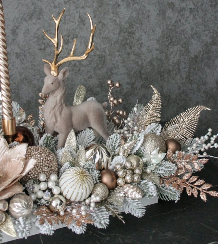 Christmas table centerpiece with a grey deer, gold ornaments, and frosted greenery.