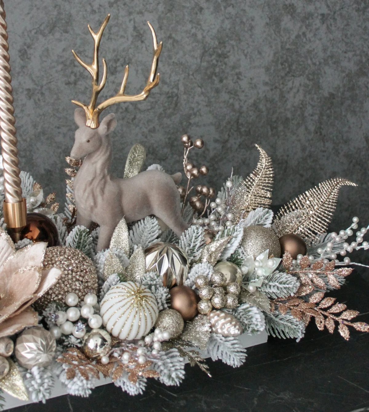 Christmas table centerpiece with a grey deer, gold ornaments, and frosted greenery.