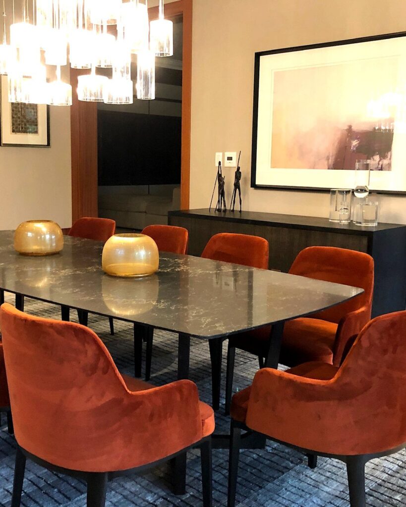 Dining room with burnt orange velvet chairs and a dark stone table.